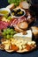 Cheese platter on a wooden board, bread, fruit and cold cuts on dark background, vertical closeup