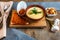 Cheese soup mashed in a clay plate is on a tray. Next to him is a piece of bread, a spoon and toast in a plate