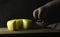 Cheese wheel with a cut piece on a wooden Board. Nearby the child`s hand takes green olives from a plate