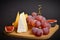 Cheeseboard platter with hard and soft mould cheese, grape and segmented fig on wooden board