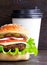 Cheeseburger on a cutting board and cup of coffee on a wooden background. Hamburger with cheese. Burger isolated. Tasty dinner