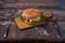 Cheeseburger with meat cutlet and pickled vegetable on a wooden cutting board on Rustic Wooden Surface with Dark Background and Co