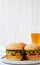 Cheeseburgers on grey plate and glass of beer. White wooden background. Side view.