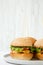 Cheeseburgers on grey plate. White wooden background. Side view.