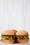 Cheeseburgers on grey plate. White wooden background. Side view.