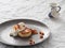 Cheesecakes or curd pancakes with cream and sea buckthorn jam on a gray plate, on a white tablecloth. Vintage gravy boat. Close-up