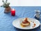 Cheesecakes or curd pancakes with cream and sea buckthorn jam on a white plate, on a blue tablecloth. Vintage gravy boat. Ð¡andle