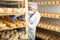 Cheesemaker in mask examining quality of cheese in ripening room