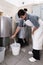 Cheesemaker opens the tap of a container to fill a bucket with fresh milk