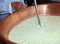 Cheesemaker stirs the curds into the cauldron to make cheese