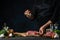 The chef adding spices on the fresh pork or beef steak on dark blue background. Concept of preparing meat. Cooking on the