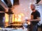 Chef in apron flaming the food in a saucepan in the kitchen of a restaurant