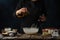 The chef in black apron pours oil into glass bowl for preparing dough. Backstage of cooking waffle on wooden table with
