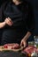 The chef in black apron pours pepper on the fresh beef steak on dark background. Backstage of preparing traditional restaurant or