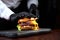 Chef in black gloves cooking a hamburger. Horizontal photo. An unrecognizable photo on a black background. Copy of the space