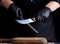 Chef in a black shirt and black latex gloves sharpen a kitchen knife on an iron sharpener with a handle