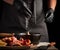 Chef in black uniform and latex gloves sprinkles with white salt raw chicken meat in a black cast-iron frying pan