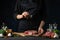 Chef in black uniform pours ground pepper on raw steak on wooden chopped board. Backstage of preparing grilled pork meat at