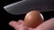 Chef breaks a raw egg with a knife on a black background close-up.