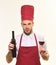 Chef in burgundy hat and apron holds bottle and wineglass.