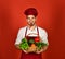 Chef in burgundy uniform holds red chili in mouth.