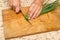 Chef chopping a green onion with a knife on the cutting board