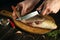 Chef cleans fresh fish on a wooden cutting board with a knife. Home cooking of a delicious fish dish according to an old recipe