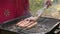 Chef cook opens lid of hot barbecue grill with chicken, pork and beef sausages and turns them over with iron tongs. Man