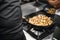 Chef cooking mushrooms in frying pan on burning fire.