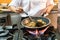 Chef Cooking Thai Food Cuisine in Skillet over Flames on Gas Stove