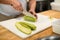 Chef cuts green zucchini with knife into pieces.