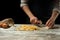 The chef cuts Italian pasta dough. Against a dark background. A concept for preparing delicious food, Italian cuisine and recipes