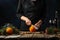 Chef cuts with knife orange on wooden chopped board for preparing mulled wine on rustic wooden table with festive composition