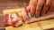 The chef cuts pieces of meat with lard on a cutting board