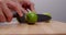 Chef cutting green lime in two pieces with knife on wood cutting board table. Hand holding and cutting lime