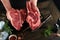 Chef cutting steak beef. Mans hands hold raw steak Tomahawk on rustic wooden cutting board on black background. Cooking