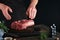 Chef cutting steak beef. Mans hands hold raw steak Tomahawk on rustic wooden cutting board on black background. Cooking