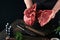 Chef cutting steak beef. Mans hands hold raw steak Tomahawk on rustic wooden cutting board on black background. Cooking,