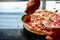 Chef is cutting yummy pizza by using pizza cutter to separate it for customer in kitchen at pizzeria.