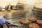 A chef with a gloved hand preparing beef burgers on a grill next to buns