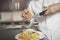 Chef Grating Cheese Onto Pasta In Kitchen