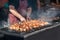 Chef grills meat skewers on a barbecue grill in a street diner