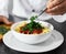 Chef, hands and bowl with pasta for fine dining, serving or cooking recipe in kitchen at restaurant. Closeup of person