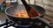 Chef mixes zucchini, tomatoes, cucumbers, sweet peppers and onions, fried in pan on gas stove