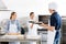 Chef Passing Baking Sheet To Colleague By Oven