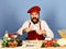 Chef with pasta, vegetables and dough on table.