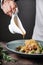 Chef plating up food in a restaurant pouring a gravy or sauce over the meat salad with potato