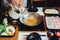 Chef is pouring clear Shabu broth in silver pot with Kurobuta pork, cabbage, eryngii, enotitake, tofu and another vegetables.