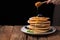 The chef pours honey pancake stack with blueberries and mint on black background. Copy space for your text