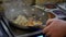 Chef pours soy and teriyaki sauces to udon noodles and fried vegetables in pan